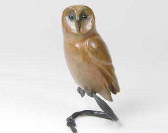 May include: A brown and black barn owl sculpture with black eyes, perched on a black metal stand.
