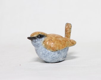 May include: A small bird figurine featuring a textured tan and brown back with wings folded against its body. The bird has a light blue chest and belly, a dark brown beak, and a distinct dark brown stripe extending from the eye area.