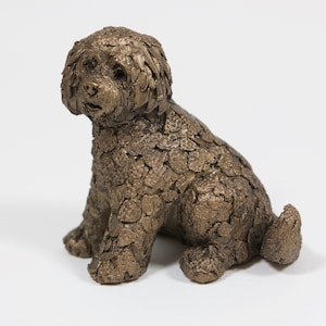 May include: A small bronze sculpture of a dog sitting with its head turned to the side. The dog's fur is textured and detailed.