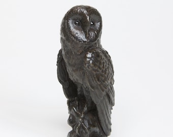 May include: A dark brown ceramic sculpture of a barn owl perched on a branch. The owl has realistic details, including feathers and eyes.