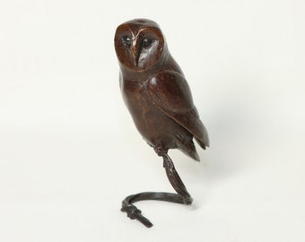 May include: A small bronze sculpture of a barn owl perched on a branch. The owl is facing forward with its wings folded. The sculpture is detailed and realistic.