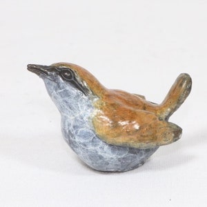 Può includere: Una piccola scultura in bronzo dettagliata di un passero solitario. L'uccello è appollaiato su uno scoglio con le ali leggermente spiegate. La scultura è dipinta in tonalità di marrone, grigio e bianco.