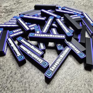 May include: A pile of black and purple rectangular objects with the text "SnoopiusMaximus" in white. Each object has a blue logo. The objects are scattered on a gray surface.
