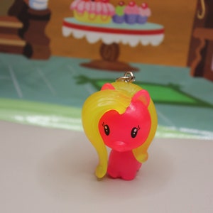 May include: A pink and yellow plastic pony keychain with a silver chain. The pony has a yellow mane and tail and black eyes.