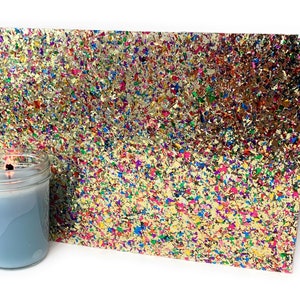 May include: A sheet of gold glitter paper with a confetti pattern in various colors, including red, blue, green, yellow, and purple. The glitter paper is on a white surface.