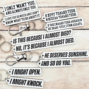 Könnte beinhalten: Schlüsselanhänger mit weißen rechteckigen Anhängern und schwarzem Text. Die Anhänger tragen Sätze wie "I ONLY WANT YOU," "I LOVE YOU SO MUCH," und "HE DESERVES SUNSHINE." Jeder Schlüsselanhänger hat einen silbernen Verschluss.