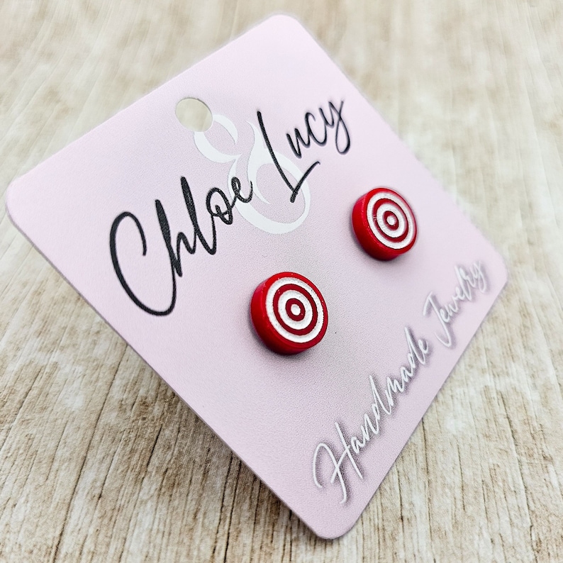 May include: A pair of red and white target-shaped stud earrings on a pink card with the text "Chloe & Lucy Handmade Jewelry".