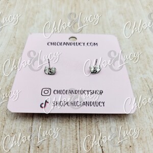 May include: A pair of silver stud earrings on a pink card with the text "Chloe & Lucy" and "CHLOEANDLUCY.COM".