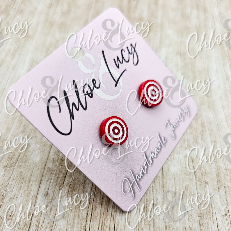 May include: A pair of red and white target-shaped stud earrings on a pink card with the text "Chloe & Lucy Handmade Jewelry".
