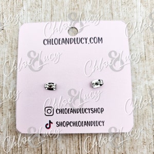 May include: A pair of silver earring backs on a pink card with the text "Chloe & Lucy" and "chloeandlucy.com". The card also includes social media icons for Instagram and TikTok.