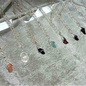 May include: A collection of silver necklaces with various gemstone pendants, including clear, green, blue, red, and black stones.