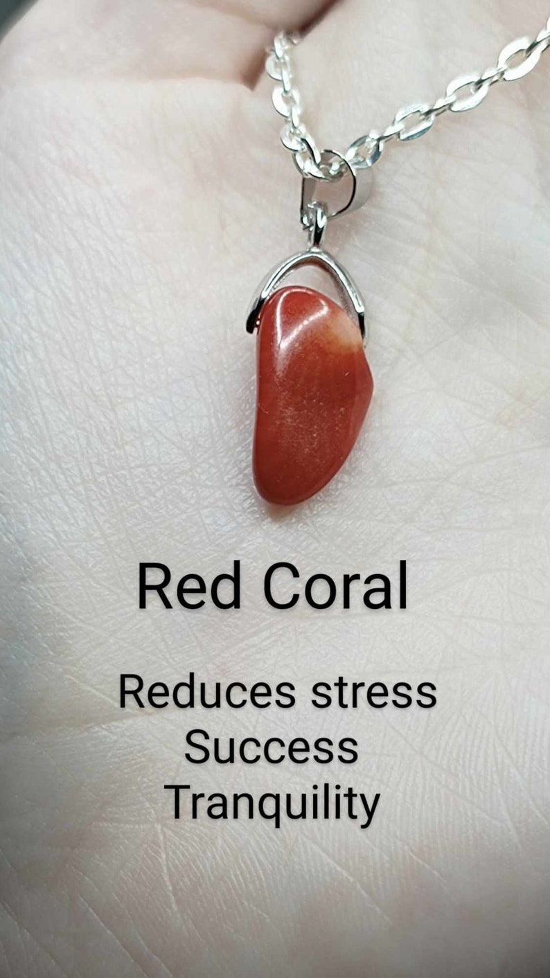 May include: Red coral pendant necklace on a silver chain. The pendant is a smooth, polished, red coral stone. The text below the pendant reads "Red Coral", "Reduces stress", "Success", and "Tranquility".