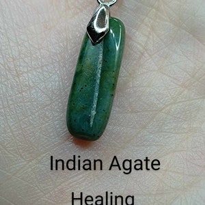 May include: A green Indian agate pendant on a silver chain. The pendant is a long, rectangular shape with a smooth, polished surface. The text below the pendant reads "Indian Agate", "Healing", "Stability", and "Courage".