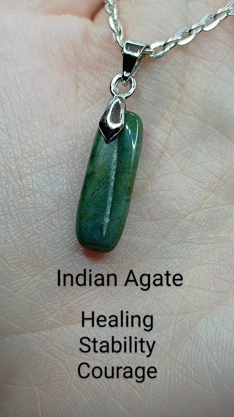 May include: A green Indian agate pendant on a silver chain. The pendant is a long, rectangular shape with a smooth, polished surface. The text below the pendant reads "Indian Agate", "Healing", "Stability", and "Courage".