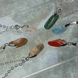 May include: Five silver necklaces with different colored stone pendants. The stones are green, blue, red, pink, and brown.
