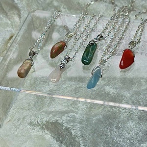 May include: Six silver necklaces with different colored stone pendants. The stones are pink, green, red, blue, and two shades of brown.