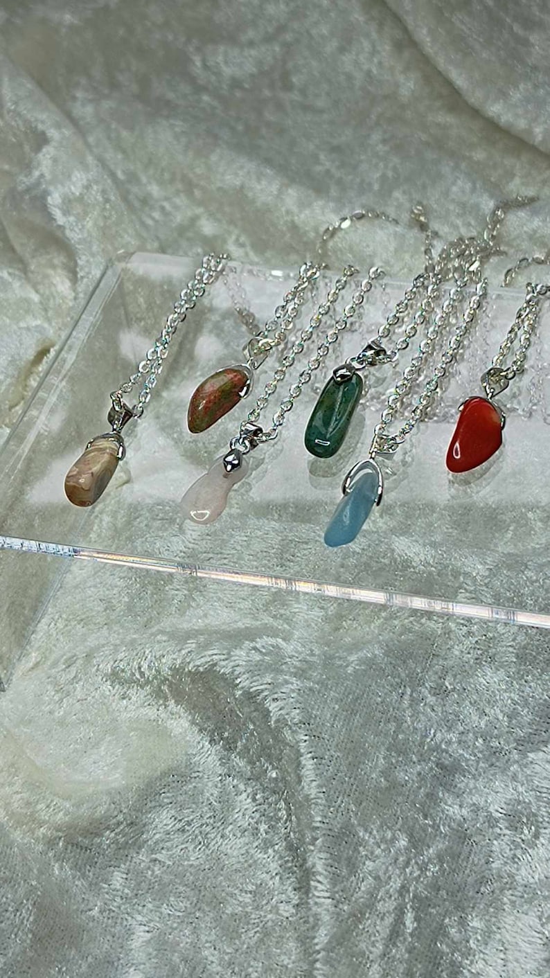 May include: Six silver necklaces with different colored stone pendants. The stones are pink, green, red, blue, and two shades of brown.