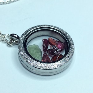 May include: A silver locket necklace with a clear glass insert containing small red and green gemstones.