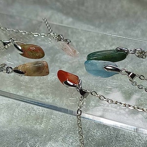 May include: Five silver necklaces with different colored gemstone pendants. The pendants are all in the shape of a teardrop and are made of agate, aquamarine, carnelian, green aventurine, and rose quartz.