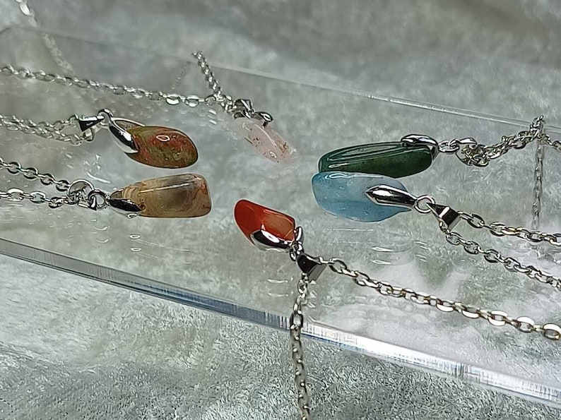 May include: Five silver necklaces with different colored gemstone pendants. The pendants are all in the shape of a teardrop and are made of agate, aquamarine, carnelian, green aventurine, and rose quartz.