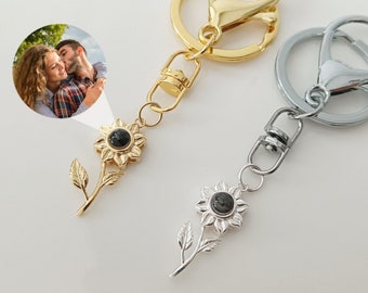 May include: Two keychains with a sunflower charm. One keychain is gold with a gold sunflower charm and the other is silver with a silver sunflower charm. Both charms have a small black photo insert in the center of the sunflower.