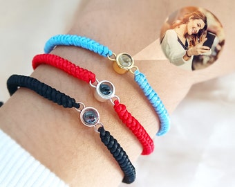 Puede incluir: Tres pulseras de la amistad con un pequeño dije redondo que revela una imagen oculta cuando se ve desde un ángulo específico. Las pulseras son rojas, negras y azul claro.
