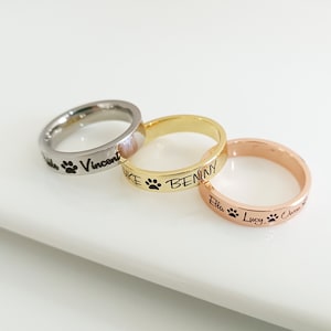 May include: Three personalised rings with engraved names and paw prints. The rings are silver, gold, and rose gold.