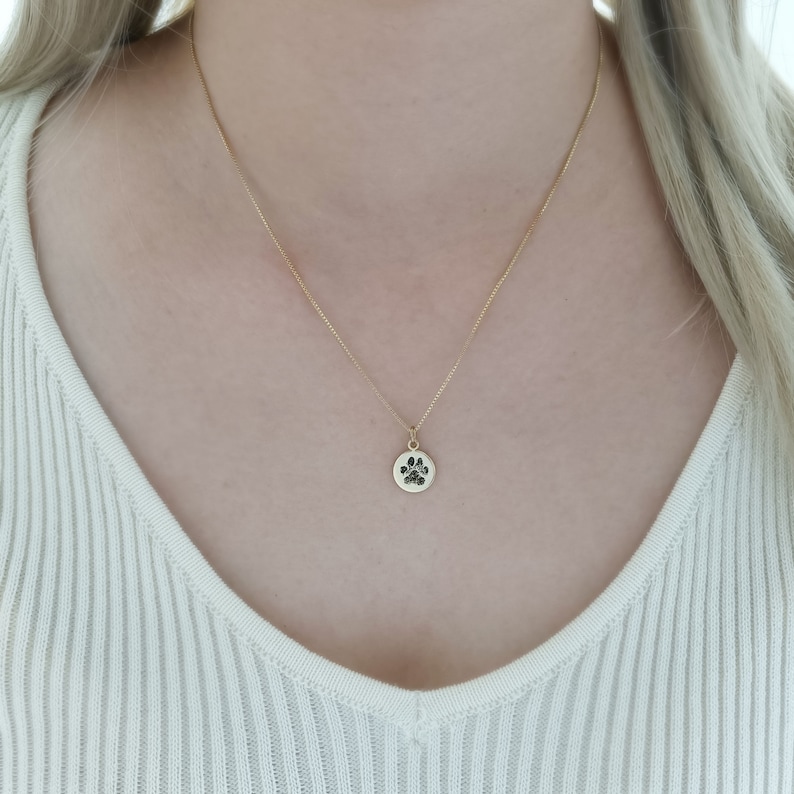 May include: A gold chain necklace with a small round pendant featuring a paw print design.