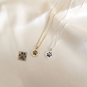 May include: Two necklaces with paw print pendants. One necklace has a gold pendant with a black paw print, the other has a silver pendant with a black paw print.