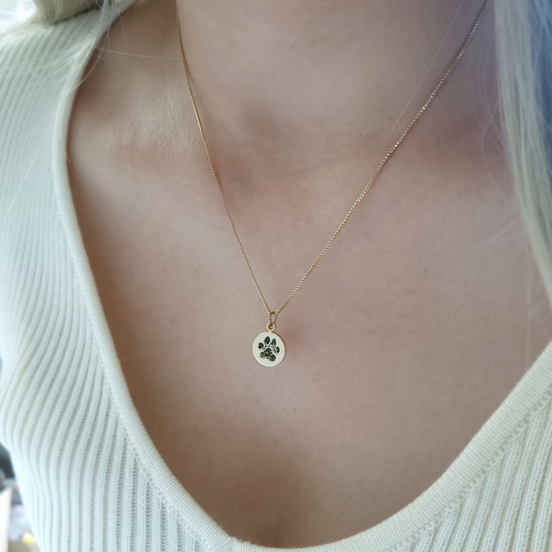 May include: A gold chain necklace with a small round pendant featuring a black paw print.