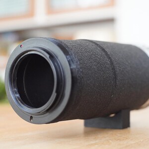 Puede incluir: Un objetivo de c&aacute;mara negro con un anillo plateado y una superficie texturizada.