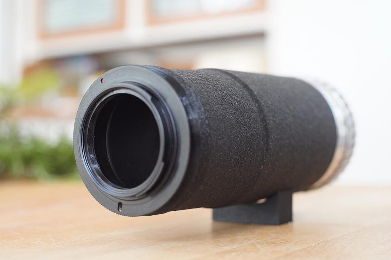 Puede incluir: Un objetivo de c&aacute;mara negro con un anillo plateado y una superficie texturizada.