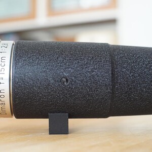 Puede incluir: Un objetivo de c&aacute;mara negro con una banda plateada que dice "Dimaron f=15cm 1:2.8".