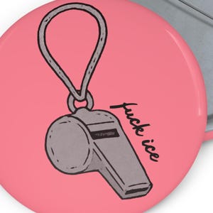 Pode incluir: Um botão redondo rosa com uma parte traseira de metal prateado. A frente apresenta um gráfico de apito cinza com um laço cinza e o texto "fuck ice" em escrita preta. Outro botão é parcialmente visível.
