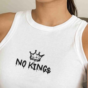 May include: White tank top with a black crown graphic and the text "NO KINGS$". The sleeveless top has a racerback design.