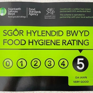 Puede incluir: Una pegatina de clasificaci&oacute;n de higiene alimentaria negra y verde con un n&uacute;mero 5 blanco en un c&iacute;rculo. El texto "DA IAWN VERY GOOD" est&aacute; debajo del c&iacute;rculo. La pegatina es de la Food Standards Agency.