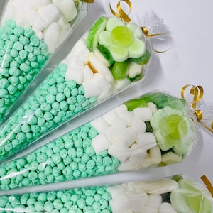 Puede incluir: Cuatro conos de pl&aacute;stico transparente llenos de caramelos verdes y blancos. Los conos est&aacute;n atados con una cinta dorada. Los caramelos incluyen caramelos de gelatina verdes, caramelos gomosos verdes, malvaviscos blancos y granulado verde.