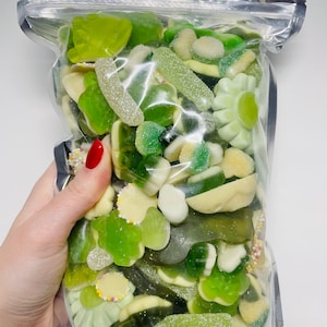 May include: A clear plastic bag filled with a variety of green gummy sweets. The sweets are shaped like flowers, leaves, and worms.