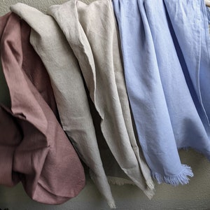 May include: Four linen tea towels hanging on a wall. The towels are in shades of brown, beige, light grey, and light blue.