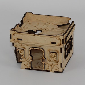 May include: A wooden model of a ruined building with a flat roof and a large window opening. The building is made of laser-cut wood and has a distressed, weathered look.