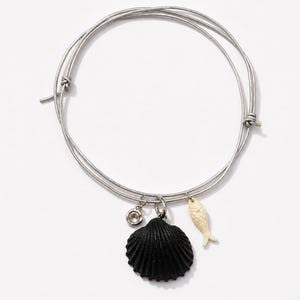 May include: A silver-toned wire bangle bracelet featuring three dangling charms: a small clear crystal, a textured black seashell, and a cream-colored fish figurine. The bracelet has a simple, adjustable circular design with thin metal wire loops.