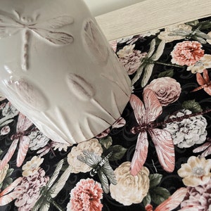 May include: A black and white table runner with a floral and dragonfly design. The runner features pink, white, and green flowers, and brown dragonflies.
