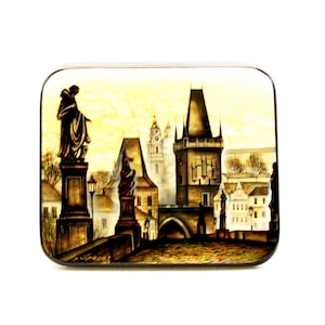 Peut inclure: Une boîte en bois peinte à la main représentant le pont Charles à Prague, en République tchèque. La boîte présente une vue de la ville avec un pont, des bâtiments et une statue. La boîte est peinte dans des tons de brun, jaune et gris.