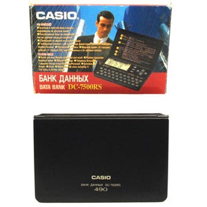 May include: A black Casio DC-7500RS Data Bank electronic organizer with a calculator keypad and display screen. The box shows a man in a suit and the text "DATA BANK DC-7500RS". The closed organizer has the Casio logo and model number.