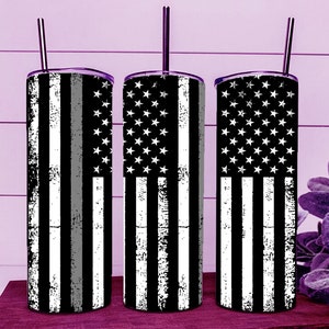 Könnte beinhalten: Drei Edelstahlbecher mit schwarz-weißem amerikanischen Flaggen-Design. Jeder Becher hat einen silbernen Strohhalm und einen schwarz-grauen Streifen. Das Design zeigt weiße Sterne und Streifen mit einem Used-Look.