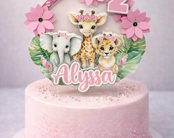 May include: A pink frosted cake with a decorative topper featuring a giraffe, lion, and elephant. The topper includes the number 2, pink flowers, and the name "Alyssa". The cake is decorated with sprinkles and a pink border.