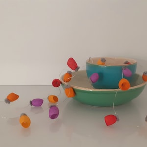 May include: A string of felt ornaments in orange, red, purple, and gray hangs between two bowls. The bowls are teal and green.