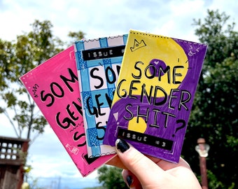 Puede incluir: Tres fanzines con portadas coloridas y títulos. El fanzine de arriba es amarillo y morado con el texto "Some Gender Shit? Issue #3". El fanzine del medio es azul y blanco con el texto "Some Gender Shit? Issue #2". El fanzine de abajo es rosa con el texto "Some Gender Shit? Issue #1".