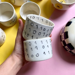 May include: Two white ceramic bowls with black handwritten numbers and symbols. The bowls are stacked on top of each other.