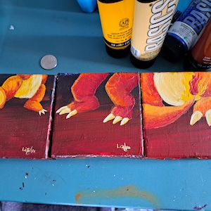Puede incluir: Tres pequeñas pinturas sobre lienzo de un dragón rojo y amarillo con garras y cola. Las pinturas están firmadas "Lisa" en la esquina inferior derecha.